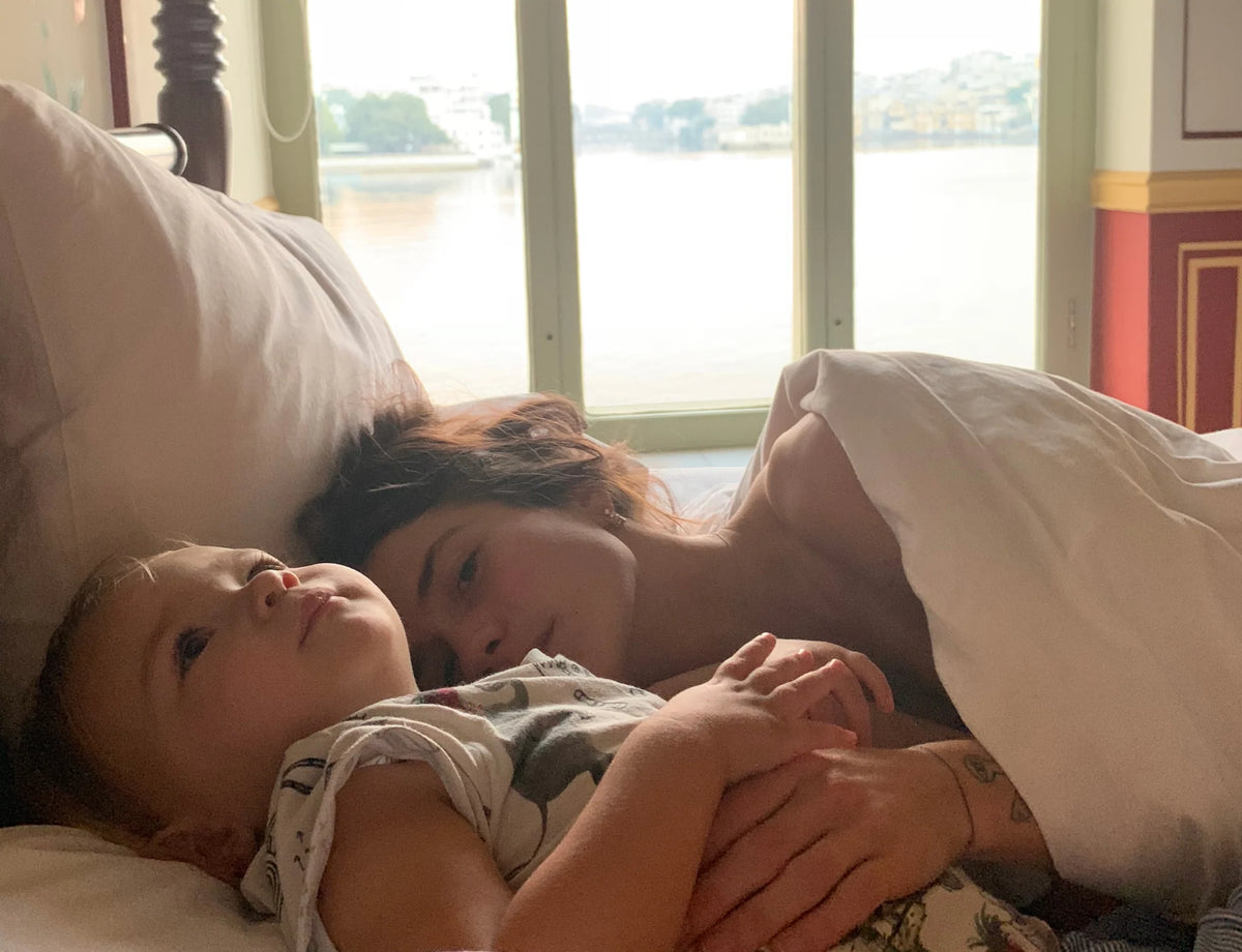 Emma Rosenzweig lying in bed with her baby in a quiet morning moment.