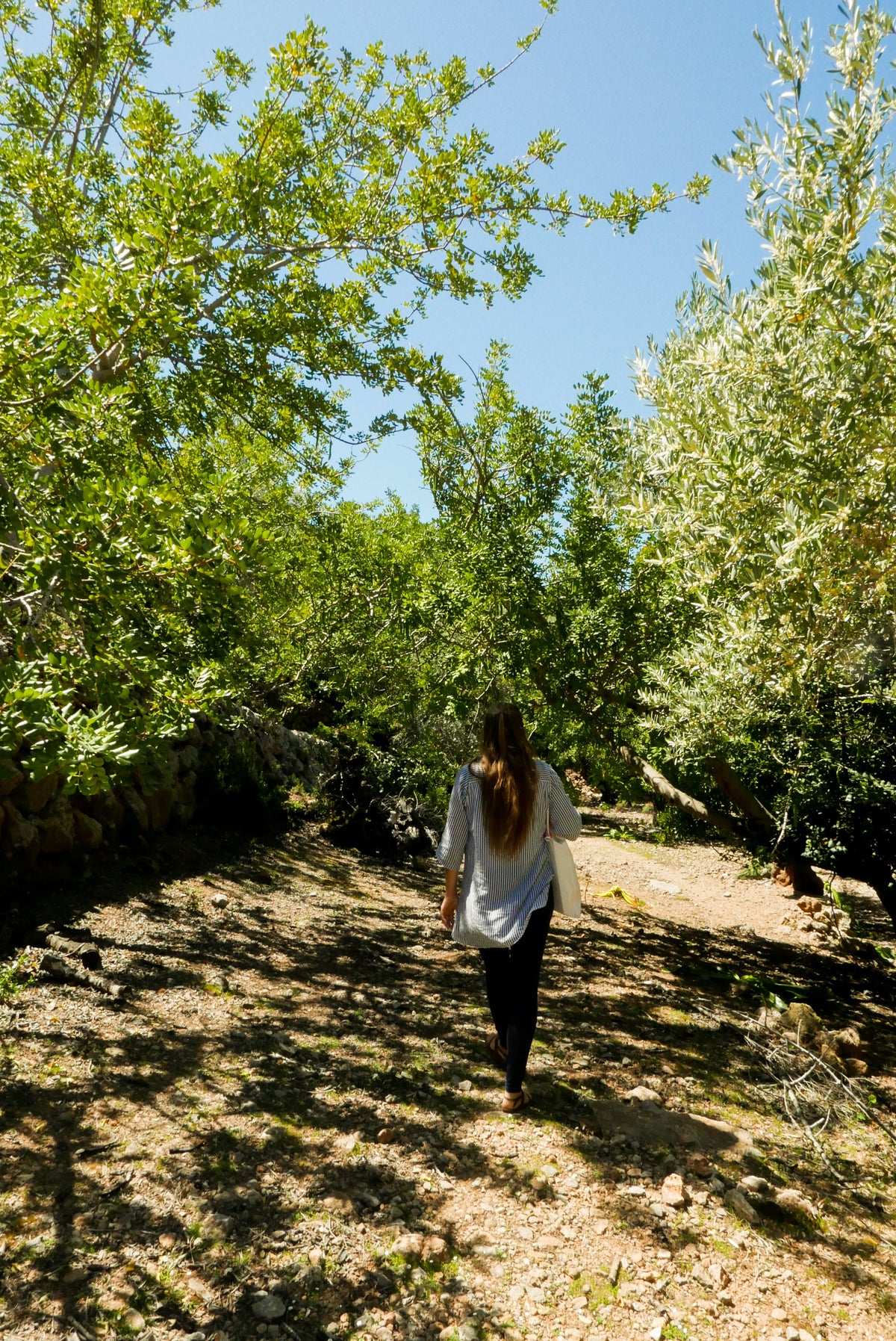 Woman walking along a shaded mountain path in Deià, Mallorca, surrounded by olive trees and lush greenery.