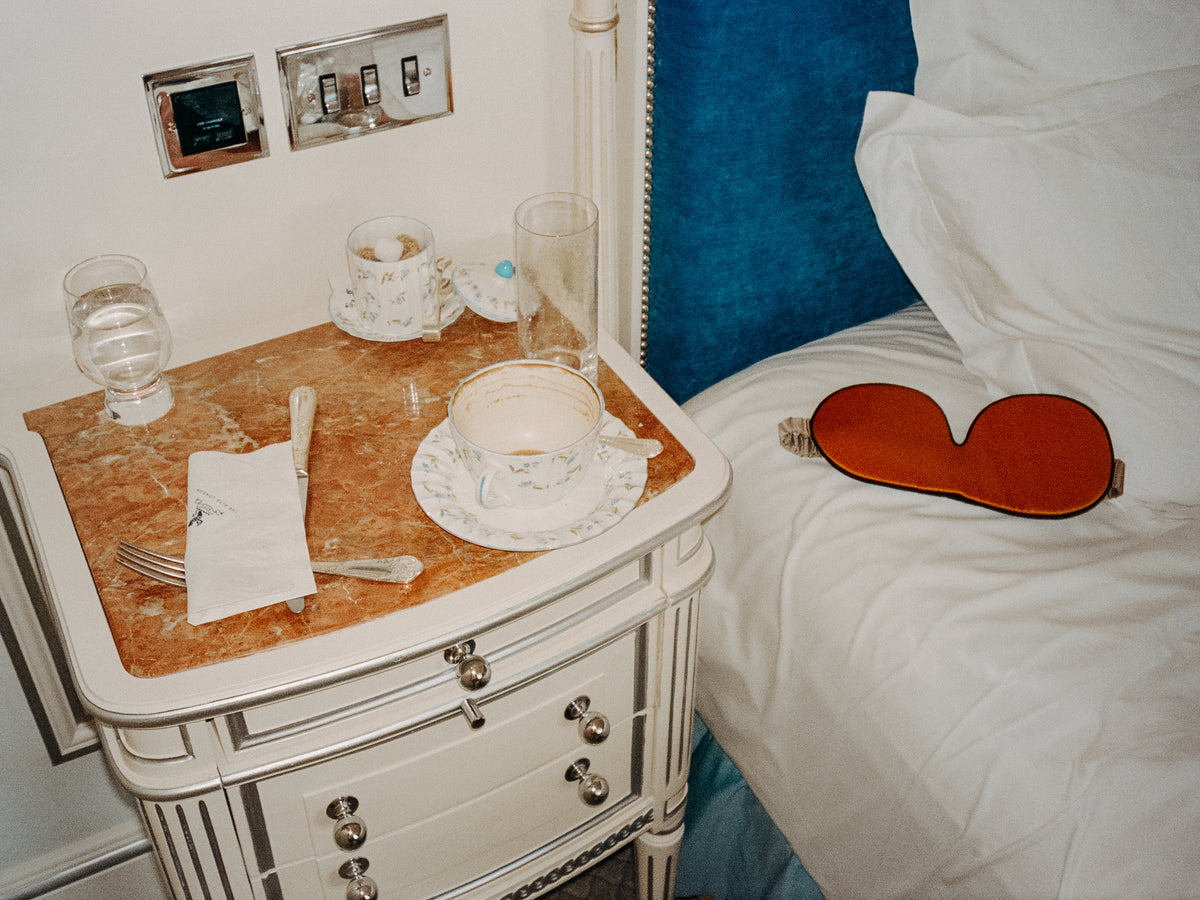 The Beauty Sleeper Golden Hour silk sleep mask on the bed, and coffee on the bedside table at the Ritz Hotel.